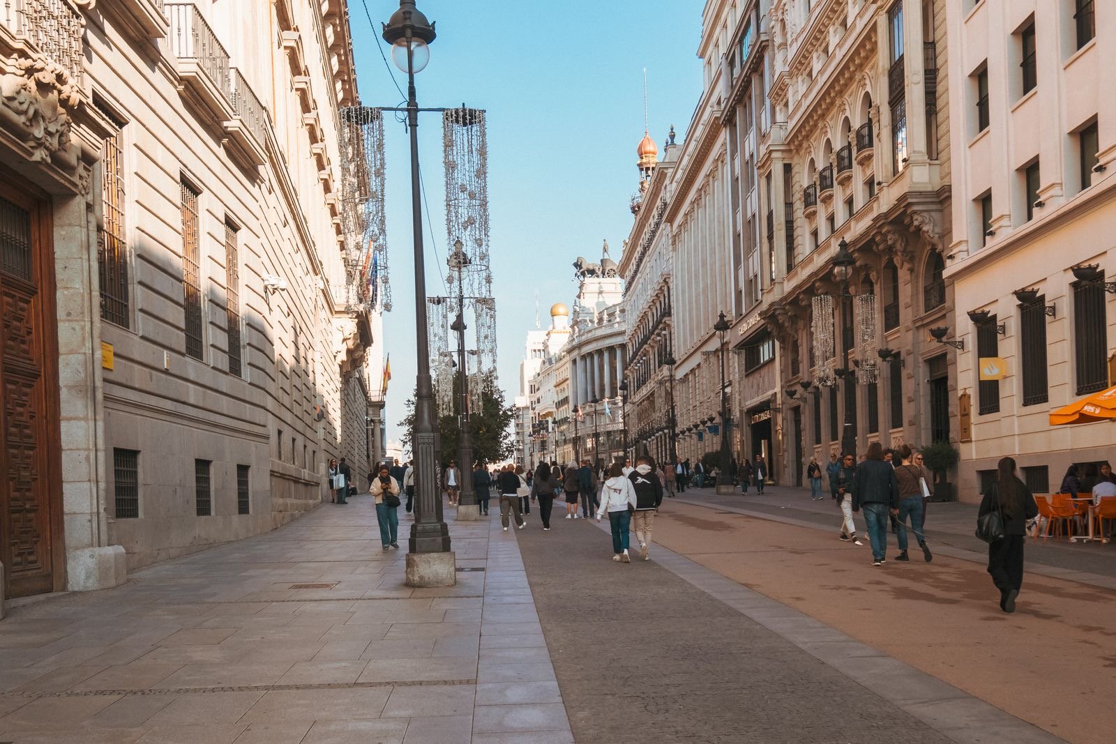 Students walking on a sunlit street beside a university campus in Spain